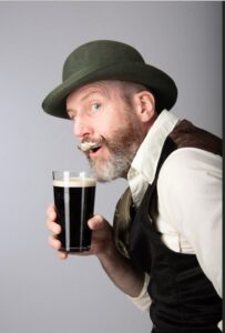 Mr Meredith is wearing a green hat and drinking a stout with foam on his curly moustache